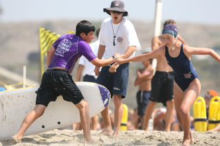 Will Rogers instructor Jonathan Wheeler (center) urges on paddler Max Babcock (left) as he tags swimmer Sara Thorson during B competition at last week's Taplin Relays at Dockweiler Beach.