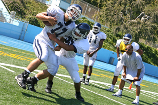 Ivan Rivera tackles David Arzumanov (left) under the watchful eye of linebackers coach Dominic Hampton during practice at Stadium by the Sea, where Palisades will host seven games this fall.