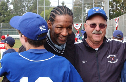 PPBA umpire Dirk Robinson hugs a Dodger player after throwing out the ceremonial first pitch on Opening Day. Commissioner Bob Benton (right) kept the duties a secret from Robinson before asking the ump to take the mound on Saturday morning in front of hundreds of onlookers. 	Photo: Rich Schmitt/Staff Photographer