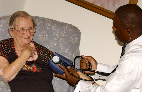 Lee takes Genevieve's blood pressure while she rests comfortably in her living room.