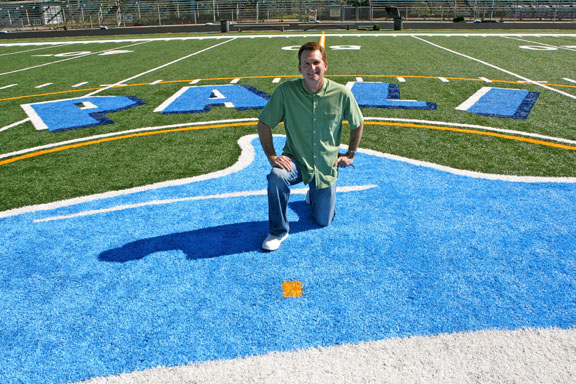 Bob Jeffers kneels on the Dolphin logo in the middle of the new synthetic turf field at Palisades High