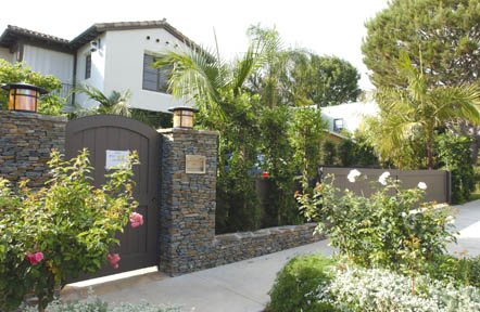 This property, located at 15204 Friends St., is the subject of a land-use dispute regarding its front-yard fence construction, including these stone pillars and the wooden pedestrian gate, which neighbors argue violate L.A. Municipal Code requirements.