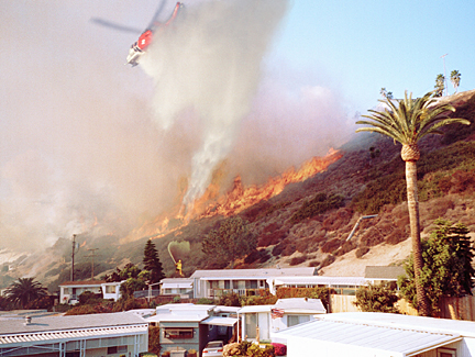 An LAFD helicopter helps attack flames burning the hillside below the Asilomar bluffs and adjacent to the Palisades Bowl mobile home park along PCH just west of Temescal Canyon Road. Photo: Jamie Budge