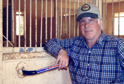 Local historian Randy Young who, along with half a dozen volunteers, stripped the interior of the 19 horse stalls in the main stable at Will Rogers last Thursday. He is pointing to one of the two remaining wrought iron horse ties that remain in the stable.