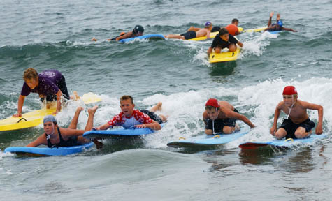 On the far left, the first person to paddle for Will Rogers C-Division, John Lemoine, appears to be behind four other paddlers. Lemoine caught a final wave, pushing him ahead of his competition and the first out of the water to make a board exchange with the second paddler.
